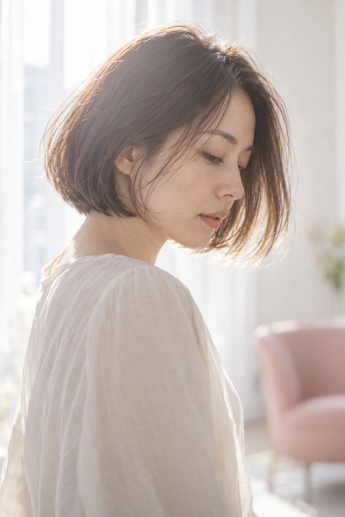切ったあと、乾かしただけでまとまったあご下のボブの女性の横顔。毛先が窓の光に透けている（写真は見本）